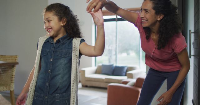 Mother and daughter having fun and dancing together in living room. Perfect for use in advertisements for family products, parenting blogs, educational materials, or lifestyle magazines focusing on family and home life.