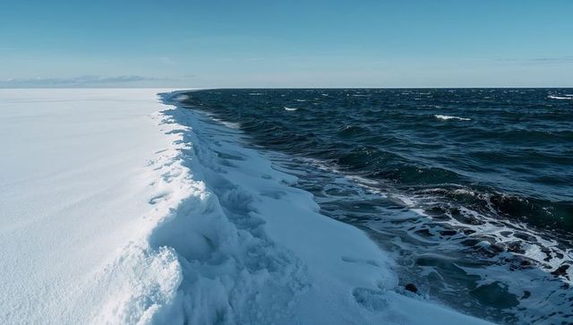 Wind-swept snow-ice ridge meeting dark arctic ocean, minimal frozen coastline horizon