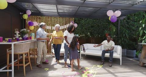 Multigenerational family celebrating birthday on backyard deck under pergola with balloons
