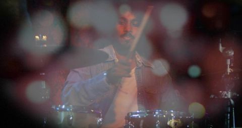 Indian drummer in denim jacket playing toms and cymbals on intimate stage with bokeh haze