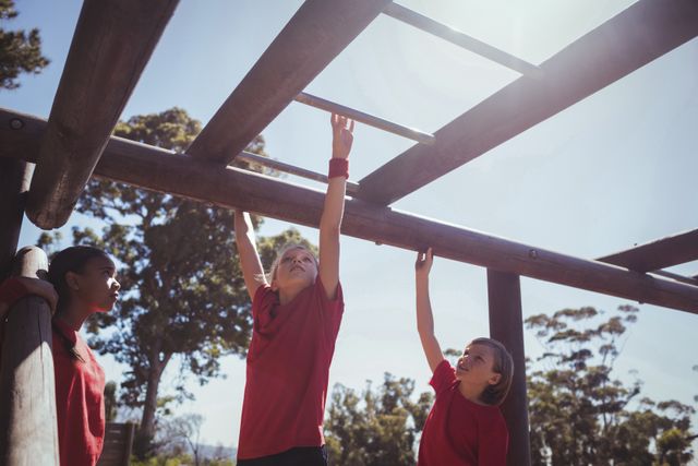 Kids in red shirts climbing on monkey bars during an outdoor boot camp. Ideal for articles on children's fitness, teamwork activities, physical education programs, and outdoor recreational activities.