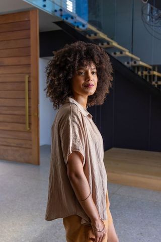 African woman standing in contemporary foyer with glass staircase, wooden door, neutral outfit