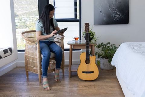 Mature woman using tablet in sunlit bedroom with acoustic guitar and houseplants