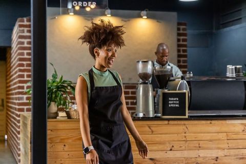 Joyful african american barista greeting customers at rustic wood counter coffee shop
