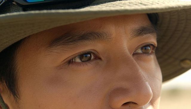 Contemplative asian man gazing outdoors wearing wide-brimmed sun hat and sunglasses
