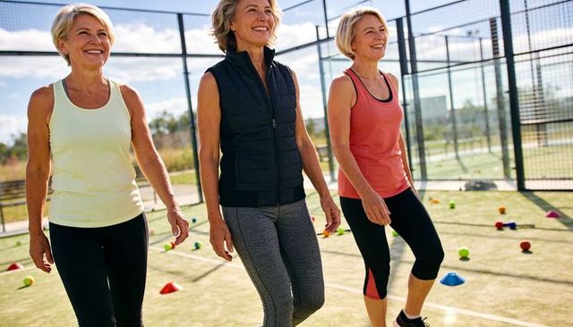 Three active mature women walking on outdoor court in sportswear, group fitness