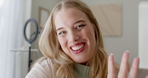Joyful blonde woman waving at home office with modern decor