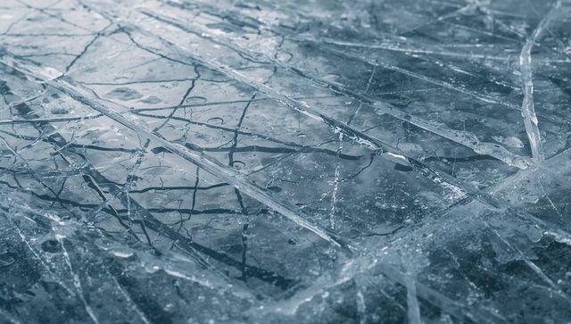 Cracked glassy ice on frozen pond with layered fractures, air bubbles and twig reflections