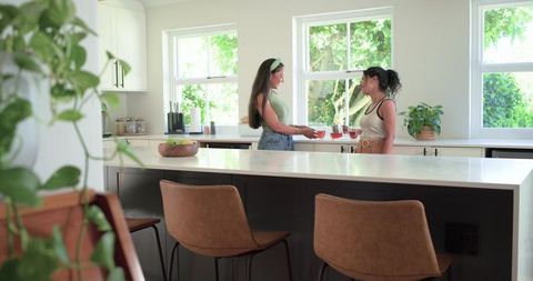 Friends Sharing Tea Over Marble Kitchen Island Amid Sunlit Greenery and Cozy Morning Chat