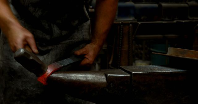 This shows a blacksmith working with red-hot metal using a hammer and anvil. Useful for visualizing traditional craftsmanship, blacksmithing techniques, and manual labor. Ideal for topics related to metallurgy, skilled trades, and historical techniques, as well as promoting craftsmanship and handmade products.