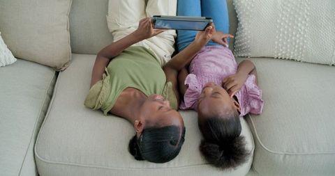 Overhead view african american sisters lying on sofa watching tablet together at home