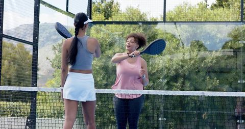African american women playing padel doubles, celebrating point on outdoor glass court