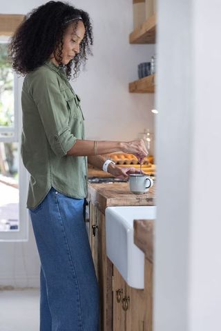 African american woman stirring mug in rustic farmhouse kitchen, calm morning routine