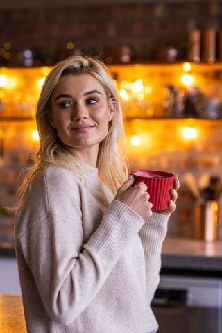 Cozy morning routine woman holding red mug in warm kitchen bokeh lights