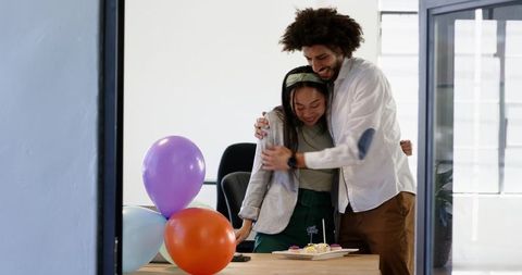 Multiracial Coworkers Hugging and Celebrating with Cupcakes and Balloons in Modern Office