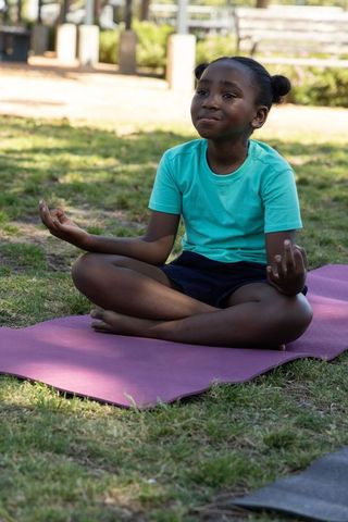 Young african american girl practicing mindfulness yoga on purple mat in park