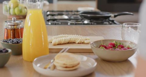 Breakfast spread showcasing stacked pancakes, fresh fruit and orange juice on wooden counter
