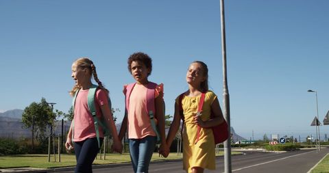 Diverse school children holding hands walking on sunny day