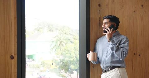 Man Holding Mug and Smartphone by Wooden Office Window