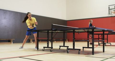 Women Engaged in Competitive Table Tennis Game in Gymnasium