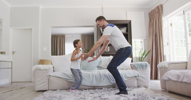 Happy caucasian father and daughter dancing together in living room. Lifestyle, domestic life, family, and togetherness.