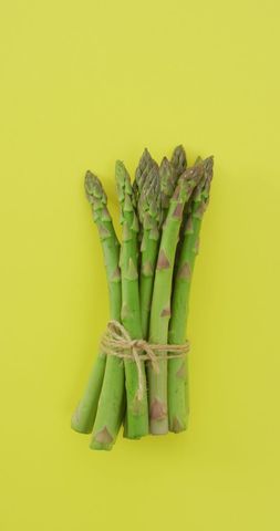 Fresh asparagus bundle on vibrant yellow background