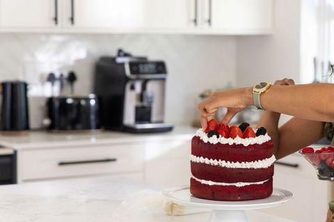 African american woman decorating red velvet layered cake with fresh berries in sunlit kitchen