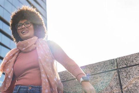 Smiling woman leaning on rooftop parapet showing smartwatch with sun flare