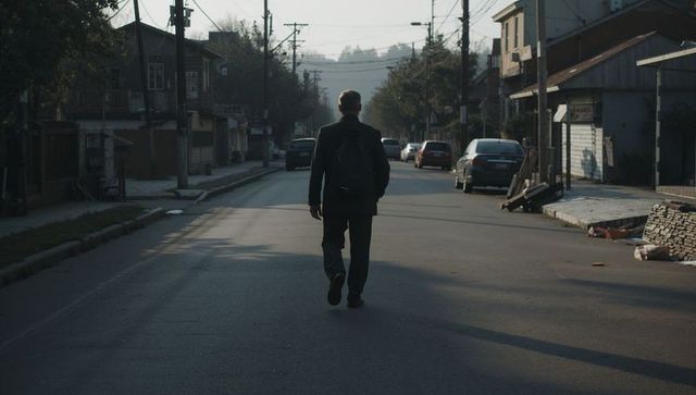 Solitary man walking down quiet suburban street at golden hour wearing backpack backlit