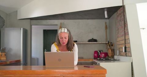 Woman working on laptop at kitchen counter with smartphone nearby, casual home office