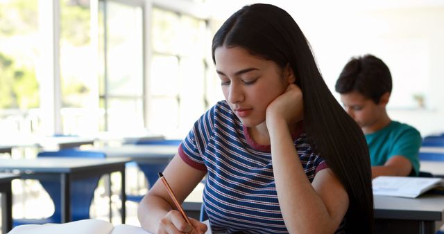 Female Student Writing in Classroom with Tablemates in Background - Download Free Stock Images Pikwizard.com