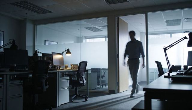 Silhouetted man walking through frosted glass office doorway in dim modern workspace