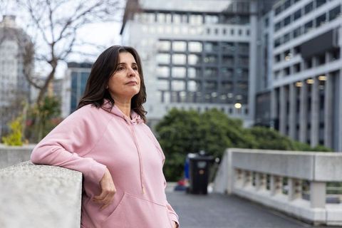 Contemplative middle-aged woman leaning on urban railing wearing pink hoodie