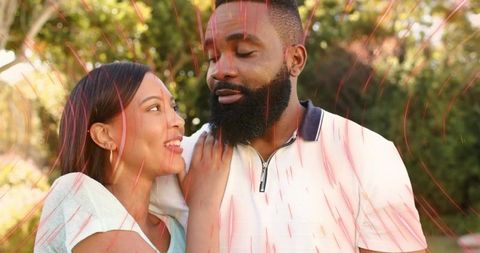 Smiling woman touching bearded man in sunlit garden sharing warm affectionate moment