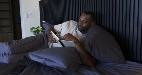 Relaxing and reading in bed with e-reader, cozy modern bedroom, evening self-care moment