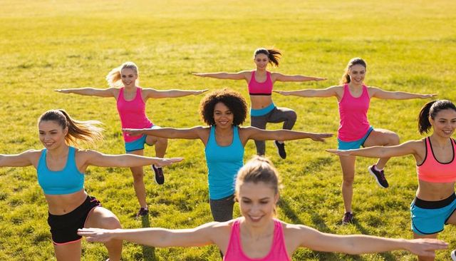 Women practicing balance in outdoor group fitness class on sunlit field