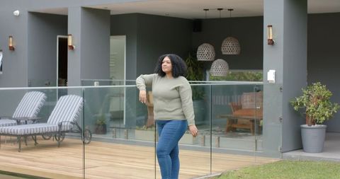 Standing on modern patio deck leaning on glass railing wearing sweater and jeans