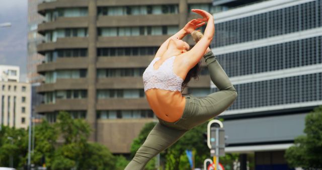 Female urban dancer executing an impressive ballet pose outdoors against cityscape backdrop. Versatile for fitness, dance, outdoor activities, city life paled in marketing, editorials, or promotional materials focusing on dance, fitness, or urban themes.