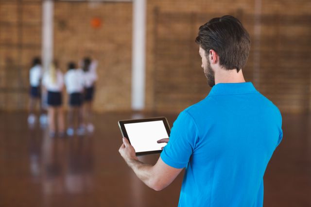Sports teacher using digital tablet in basketball court at school gym