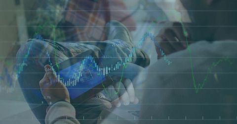 Man holding tablet studying candlestick market charts while collaborating on laptop