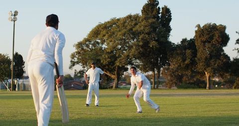 Playing cricket on sunlit suburban field in white uniforms, bowler bowling and batsman batting
