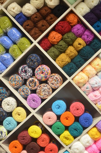 Colorful balls of yarn are neatly arranged on a shelf, organized by colors. This vibrant display is perfect for materials related to crafting, knitting, crocheting, textiles, DIY projects, and wool collection. Ideal for promoting handmade crafts, textile stores, or creative hobbies.