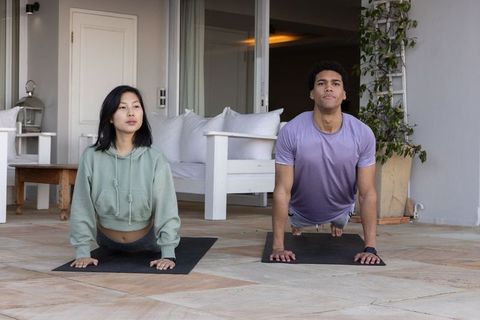Diverse fitness partners practicing yoga outdoors on tiled patio