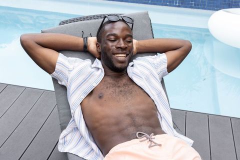 African american man reclining on poolside lounge chair, smiling and relaxing