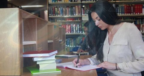 Female Student Writing Notes in Library Study Carrel Surrounded by Textbooks