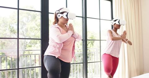 African American women practicing VR yoga balancing on one leg in sunlit studio in pink activewear
