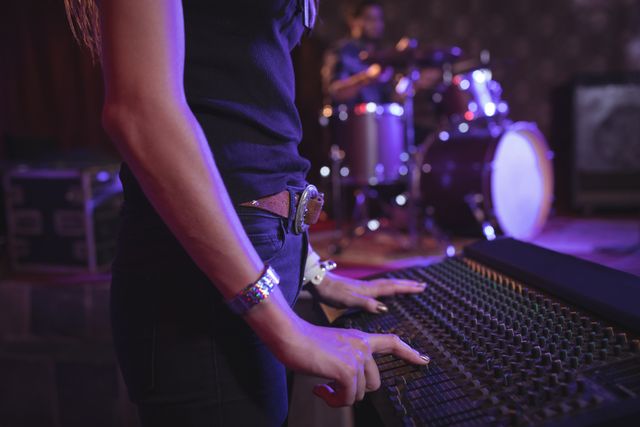 Female musician adjusting sound mixer during live performance in nightclub. Ideal for use in articles or advertisements related to music production, live concerts, nightlife entertainment, and sound engineering. Can also be used for promoting audio equipment and technology.