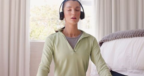 Woman meditating with headphones in peaceful bedroom setting