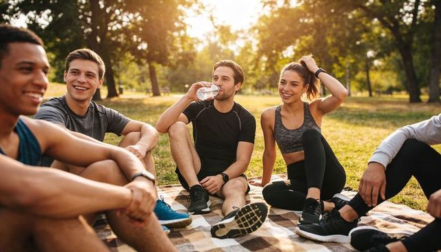 Friends cooling down and drinking water after workout on park lawn at golden hour