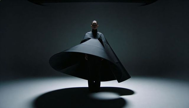 Model wearing sculptural black cone cape casting dramatic circular shadow in studio